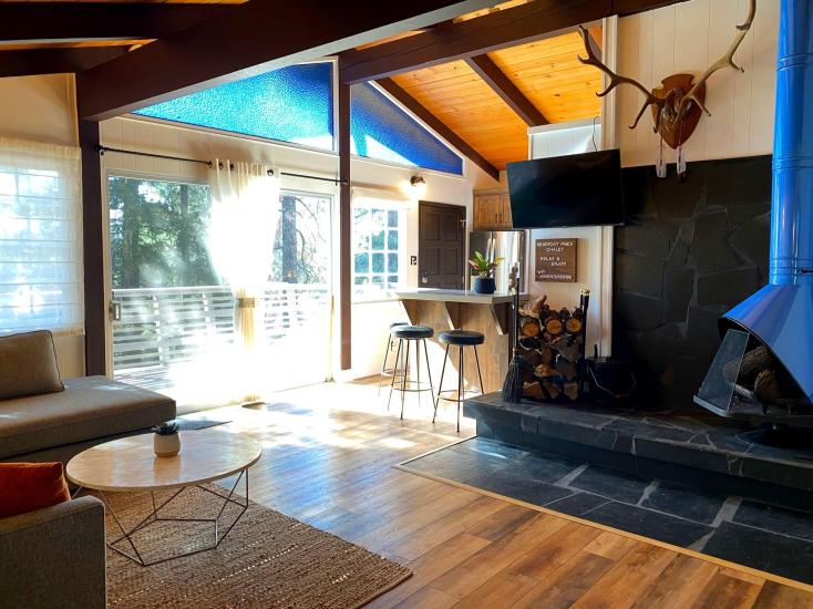 An interior shot of a Clean Sheets cabin - there are large windows showing the deck and trees bathed in sunlight outside.