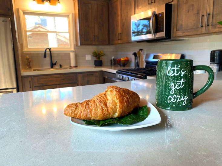 An interior shot of a cabin kitchen with a croissant on a counter next to a green mug - the stove and sink are out of focus.