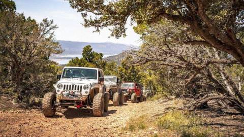 Three Jeeps climbing up a dirt off-roading trail - Big Bear's lake, mountains, and forest are visible in the background.