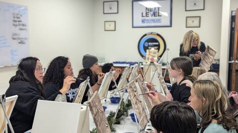 A group of painters learning how to draw natural scenery, the teacher is standing up and guiding them as she continues.