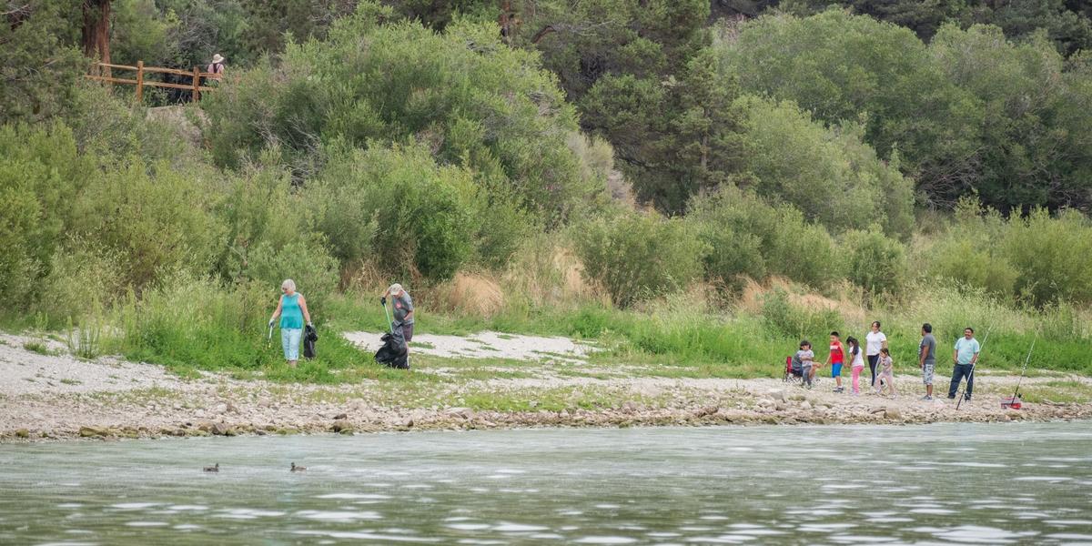 A pair of volunteers on the lakeside picking up trash with their grabbers to Care For Big Bear.