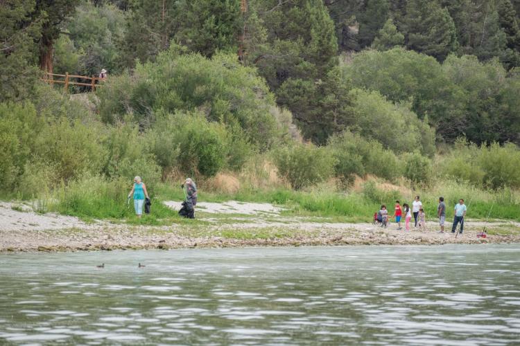 A pair of volunteers on the lakeside picking up trash with their grabbers to Care For Big Bear.