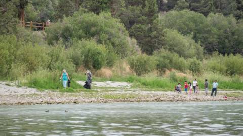 A pair of volunteers on the lakeside picking up trash with their grabbers to Care For Big Bear.