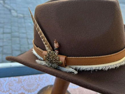 A custom hat made by Lucky Baldwin's - the leather brown colored hat is decorated with a feather sticking up on the side.