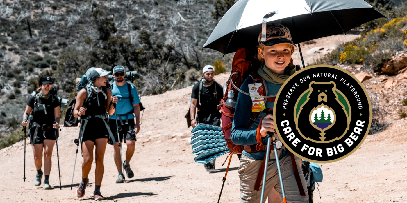 A group of hikers talking and laughing while trekking on, the Care For Big Bear logo is display off to the side.