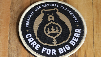 A woven patch of the Care For Big Bear logo stating to preserve our natural playground.