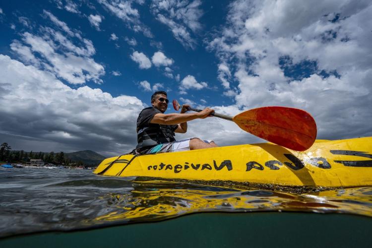 A man smiles as he paddles a yellow kayak on the water at Big Bear Lake.