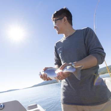 a man holding a freshly caught trout while fishing on a sunny day in Big Bear Lake