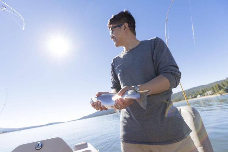 a man holding a freshly caught trout while fishing on a sunny day in Big Bear Lake