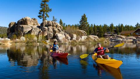 A couple holding paddles while sitting in kayaks on the lake waters - Boulder Bay Island is visible in the background.