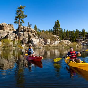 A man in a yellow kayak and woman in a red kayak on Big Bear Lake on a sunny summer day
