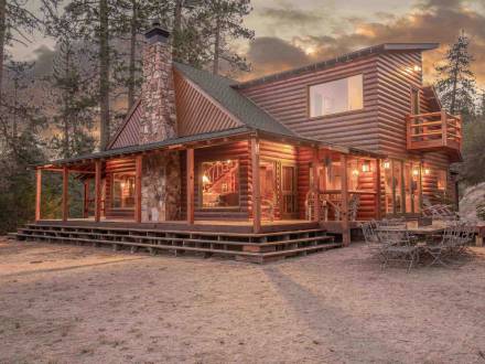 A Maltby Cabin in the forest sporting a rich wooden exterior with a stone chimney and crystal clear glass panes.
