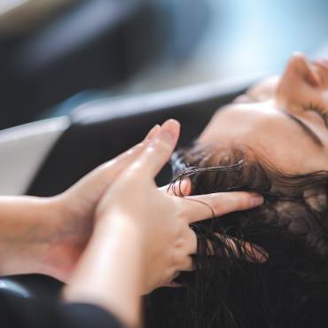 A photo of a lady having her hair washed at a salon, the barber's fingers massaging her scalp.