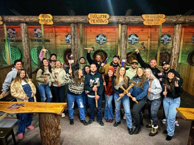 A group of people holding throwing axes at Yosemite Axe Throwing while posing for the camera - the targets are behind them.