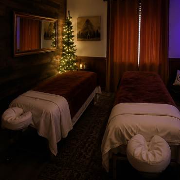 Two long massage tables in a room gently illuminated by mood lighting - the massage tables have plush covers and headrests.