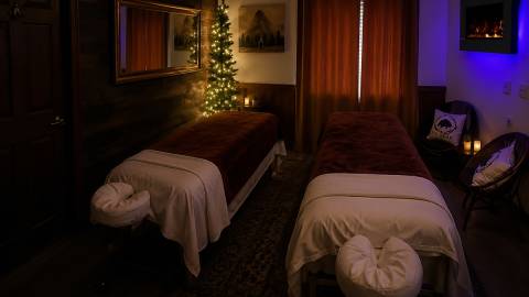 Two long massage tables in a room gently illuminated by mood lighting - the massage tables have plush covers and headrests.