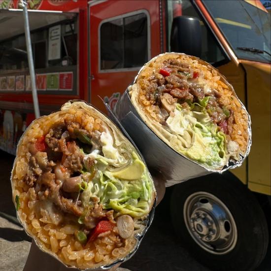 A photo of TACOTAOS burrito there is rice, meat, and beans. Their food truck is visible in the background with a sunshade.