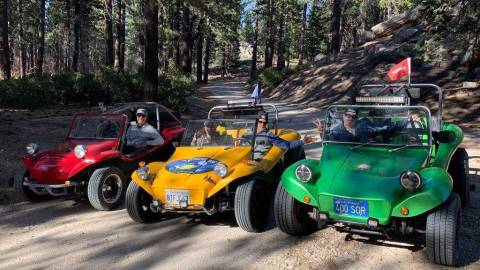 Three buggies lined up on a dirt off roading trail, the people inside them are posing for a photo.