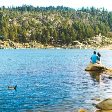 A couple sits on a rock by the lake shore