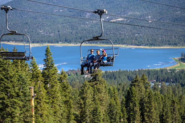 A family of three enjoying a ride on the Sky Chair overlooking the beautiful Big Bear Lake and the valley in the background.