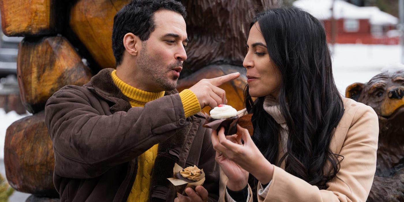 A photo of a couple sitting in front of a snow covered bear statue whilst sharing tastes of their cupcakes.