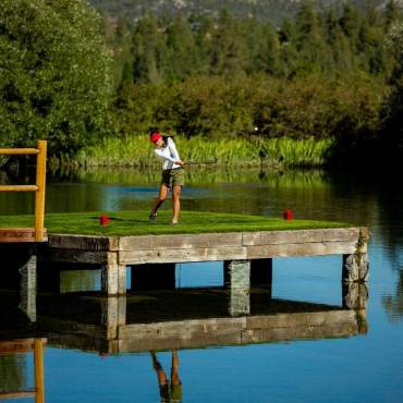 A photo of a lady in the middle of a swing at the Bear Mountain Golf Course, the platform under her is floating above a pond.