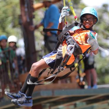 A photo of a boy strapped in securely for Ziplining with Action Zipline Tours, he is wearing thick gloves and a helmet.