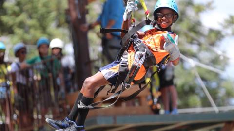 A photo of a boy strapped in securely for Ziplining with Action Zipline Tours, he is wearing thick gloves and a helmet.