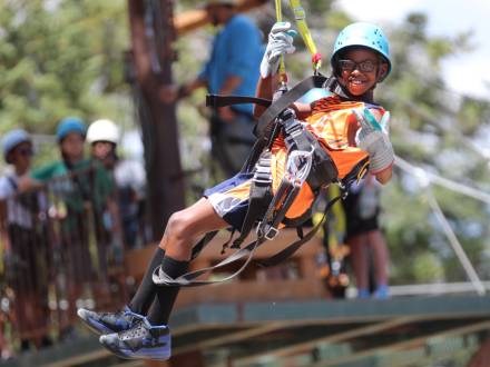 A photo of a boy strapped in securely for Ziplining with Action Zipline Tours, he is wearing thick gloves and a helmet.
