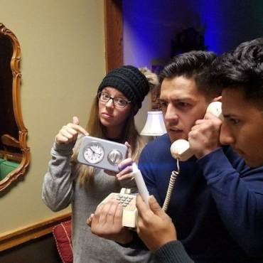 Three friends — one holding a clock and another holding a phone — solve their way out of an escape room in Big Bear Lake, CA