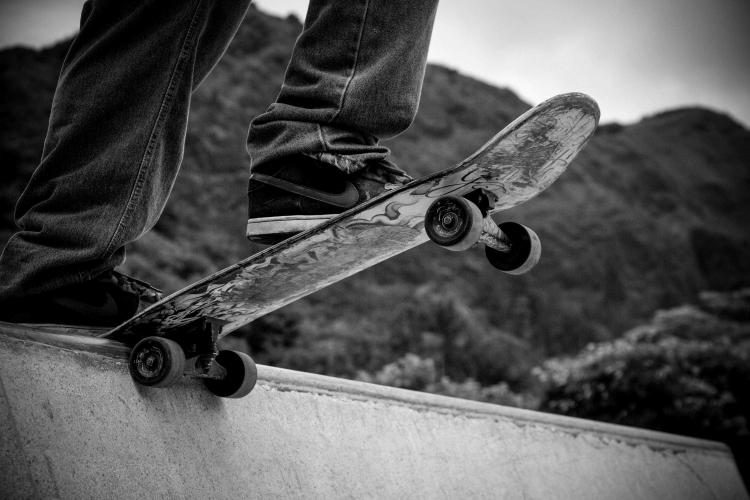 A black and white photo of a person riding a skateboard on the edge of a small wall, the mountains visible behind him.