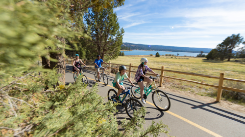A photo of a family of four riding their bikes along a narrow road, the Big Bear Lake visible in the distance.