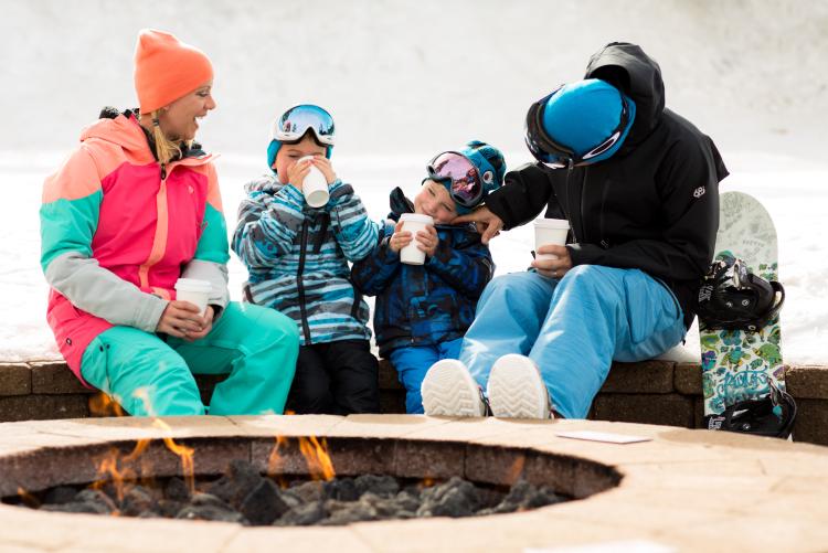 A family sips cocoa around a fire pit
