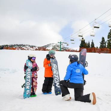 A photo of two young snowboarders learning how to snowboard from an instructor at Bear Mountain Ski Resort.