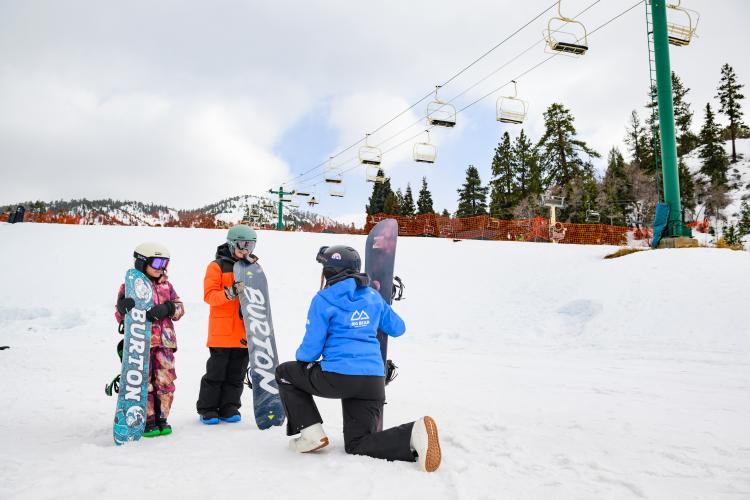 A photo of two young snowboarders learning how to snowboard from an instructor at Bear Mountain Ski Resort.