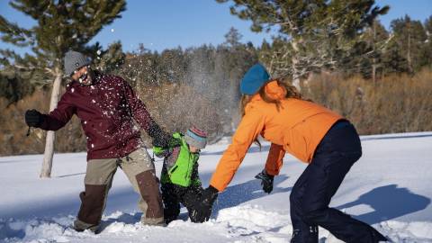 A family of three play in the snow during winter in Big Bear Lake.