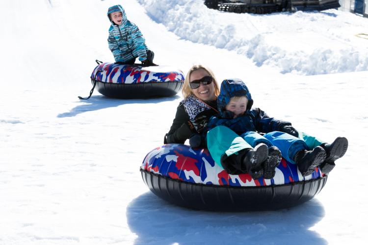 A mom and child slide down a snowy hill while tubing in Big Bear Lake in winter.