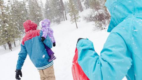 A family carries their child and a sled into a snowy area to enjoy fresh snowfall in Big Bear Lake