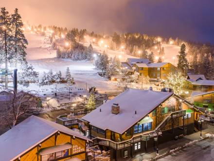 Snow Summit is illuminated at night for night skiing sessions during the winter season. Snow covers the buildings and trees.