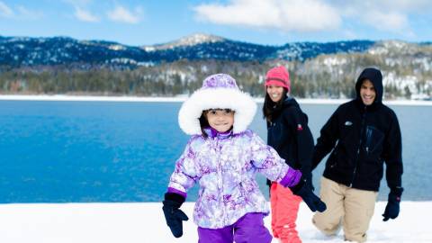 A child, bundled up in snow gear, walks through the snow ahead of her parents during winter in Big Bear Lake.