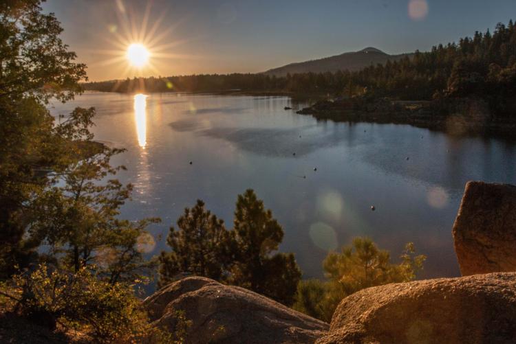 A photo of Big Bear Lake, the sunset gently illuminating the lake and mountains, the water reflecting the beach like a mirror