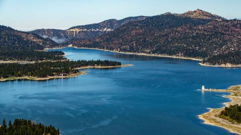 An aerial view of Big Bear Lake. It is a sunny day, with clear blue skies and green pine forests surround the blue lake.