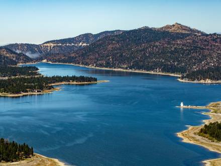 An aerial view of Big Bear Lake. It is a sunny day, with clear blue skies and green pine forests surround the blue lake.