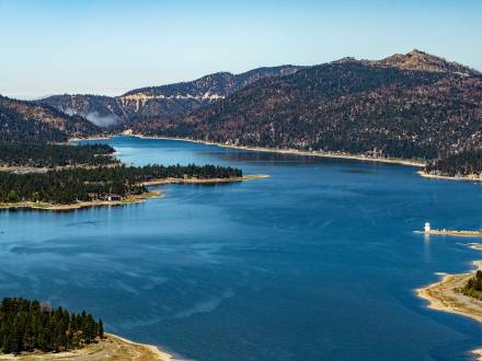 An aerial view of Big Bear Lake. It is a sunny day, with clear blue skies and green pine forests surround the blue lake.