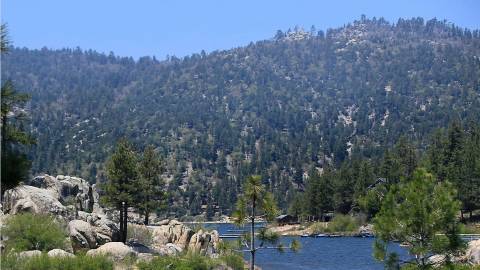 A photo of the lake behind two small boulder and tree covered hills, the mountains visible in the distance.