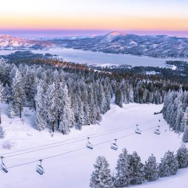 An overhead photo of the snow covered skiing hills, the Big Bear Lake, and the mountains gently reflecting the sunset.