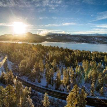 The sun shines over Big Bear Lake, a forest and a winding road following a recent falling of snow in Big Bear, CA.