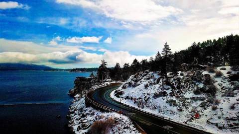 Winter driving in Big Bear Lake California with a windy snow-filled road amidst blue skies and evergreen trees
