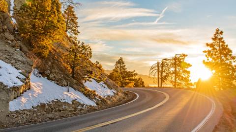 A Spring Sunrise in Big Bear Lake - there is a light amount of snow on the left side of the road curving out of view.