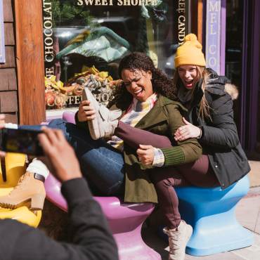 A male taking a photo of two ladies posing while sitting on the hand styled chairs at the Village Sweet Shop
